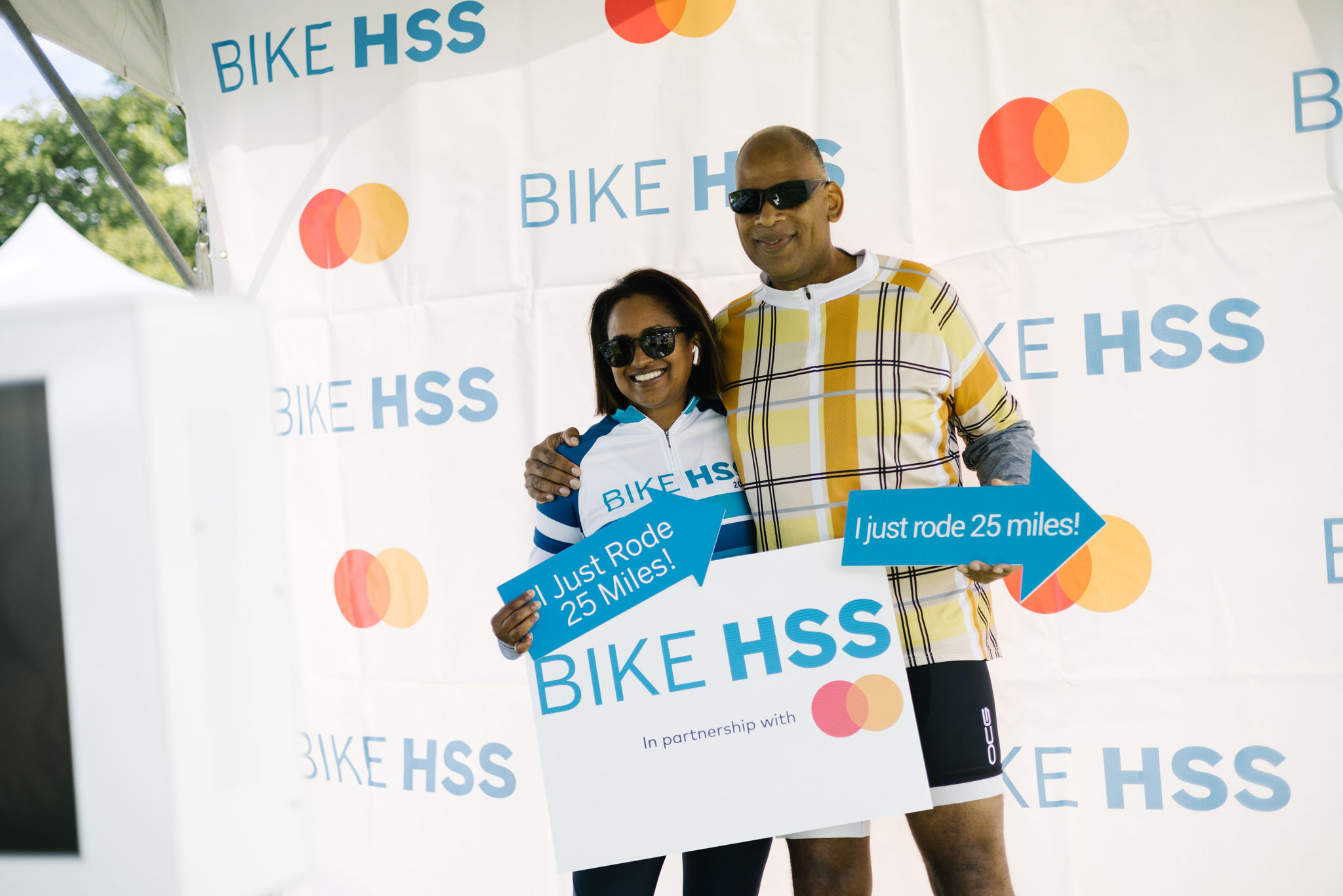 A couple smiling while posing for a photo with a bike and a sign.