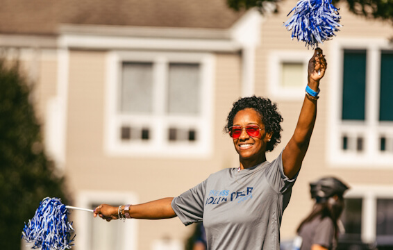 Volunteer smiling and raising her arms with pom poms
