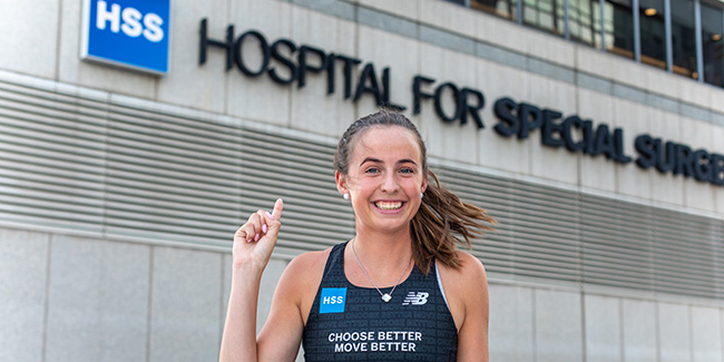 Photo of marathon runner smiling pointing at HSS sign